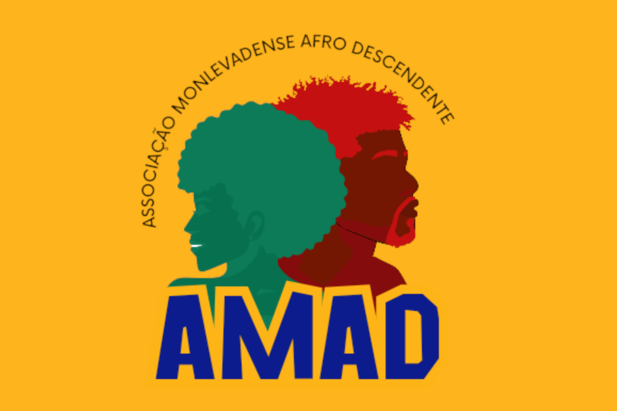 Logotipo da AMAD – Associação Monlevadense Afro Descendente, sobre fundo amarelo. No centro, há as silhuetas de duas pessoas negras: à esquerda, uma mulher em verde com cabelo afro, voltada para a direita; à direita, um homem em vermelho com barba e cabelo crespo, voltado para a esquerda. Acima das figuras, em semicírculo, está escrito “ASSOCIAÇÃO MONLEVADENSE AFRO DESCENDENTE” em letras pretas. Abaixo, em destaque, aparece a sigla "AMAD" em letras maiúsculas azuis com caixo, o texto "AMAD" em letras roxas.